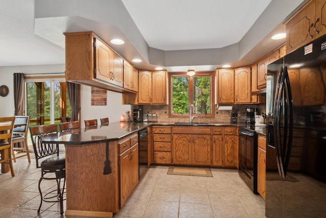 kitchen with black appliances, a sink, dark countertops, a peninsula, and decorative backsplash