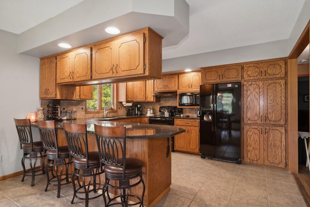 kitchen with dark countertops, backsplash, a peninsula, black appliances, and a sink