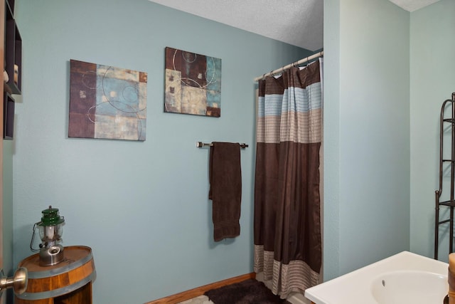 bathroom featuring a shower with curtain, baseboards, and a textured ceiling