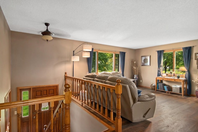living area featuring a textured ceiling, wood finished floors, baseboards, and ceiling fan