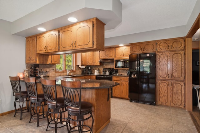 kitchen featuring black appliances, a peninsula, dark countertops, a sink, and backsplash