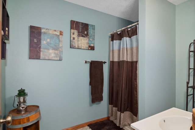 bathroom featuring a shower with shower curtain, baseboards, and a textured ceiling