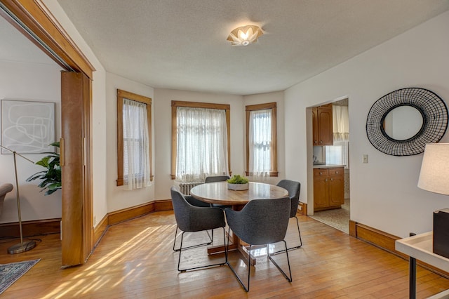 dining area with baseboards, light wood-style floors, and a textured ceiling