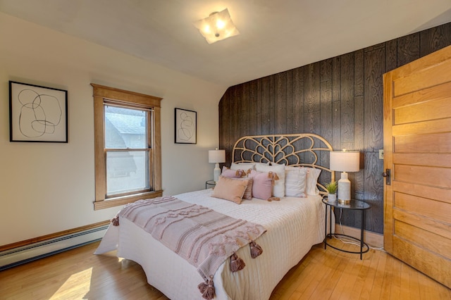 bedroom featuring wooden walls, light wood finished floors, and a baseboard radiator