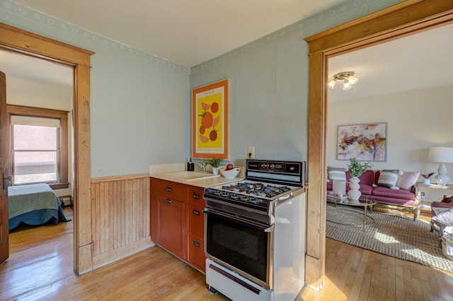 kitchen featuring a wainscoted wall, gas stove, light wood-type flooring, and a sink