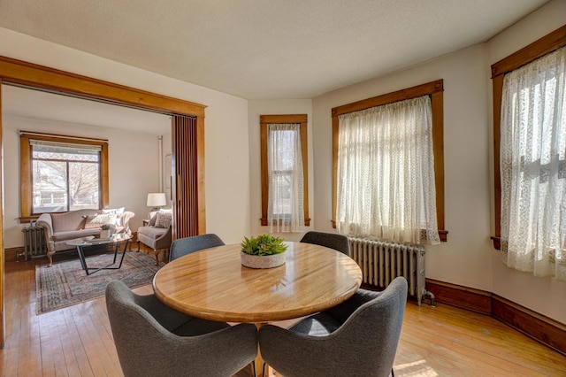 dining area with baseboards, radiator heating unit, and light wood-style floors