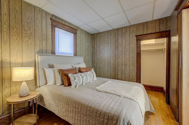 bedroom with a drop ceiling, wooden walls, a closet, and wood finished floors