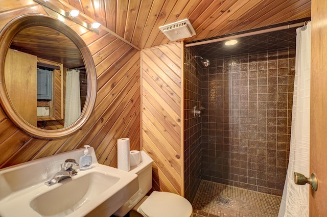 full bathroom with a tile shower, wooden walls, toilet, and a sink