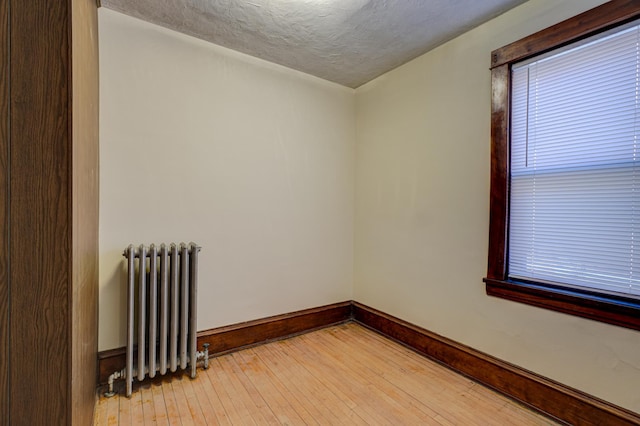 unfurnished room with radiator heating unit, baseboards, light wood-type flooring, and a textured ceiling