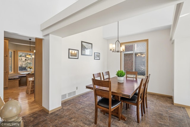 dining space with a notable chandelier, baseboards, visible vents, and stone finish flooring