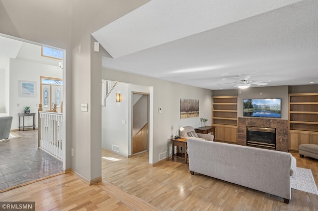 living area featuring visible vents, baseboards, ceiling fan, a tiled fireplace, and light wood-type flooring