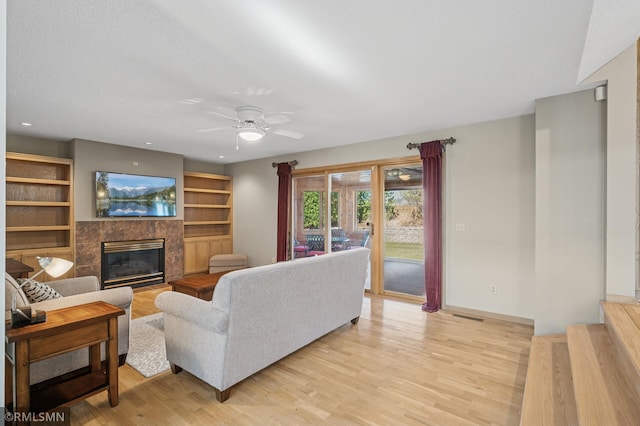 living area featuring a fireplace, light wood-style floors, baseboards, and ceiling fan