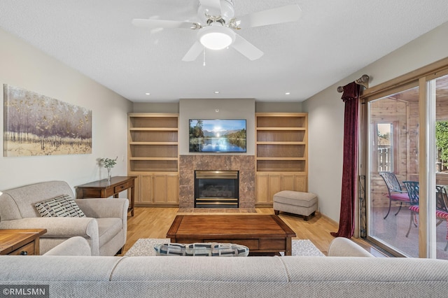 living room with a fireplace, a textured ceiling, ceiling fan, and wood finished floors