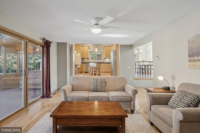 living room featuring light wood finished floors, a textured ceiling, and a ceiling fan