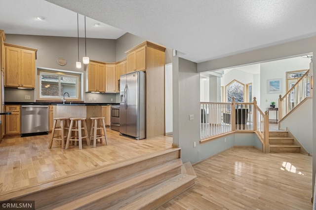 kitchen featuring light wood-type flooring, a breakfast bar, light brown cabinets, dark countertops, and stainless steel appliances