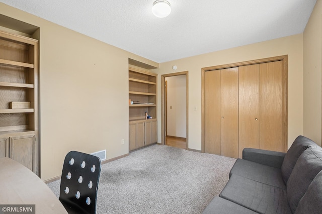 carpeted office space featuring built in features, visible vents, baseboards, and a textured ceiling