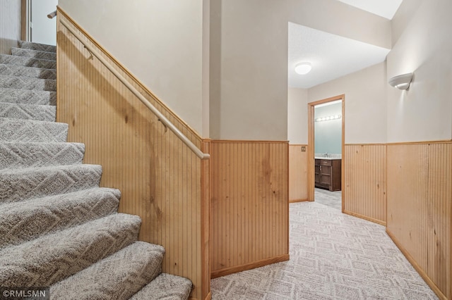 staircase featuring carpet floors, wooden walls, and wainscoting