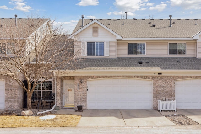 multi unit property with brick siding, a garage, driveway, and roof with shingles