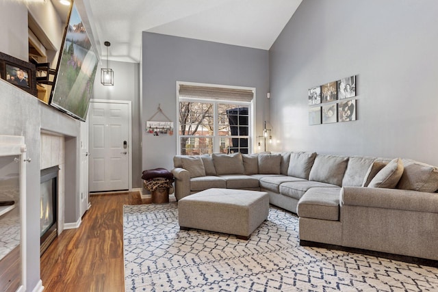 living area with a tile fireplace, high vaulted ceiling, baseboards, and wood finished floors