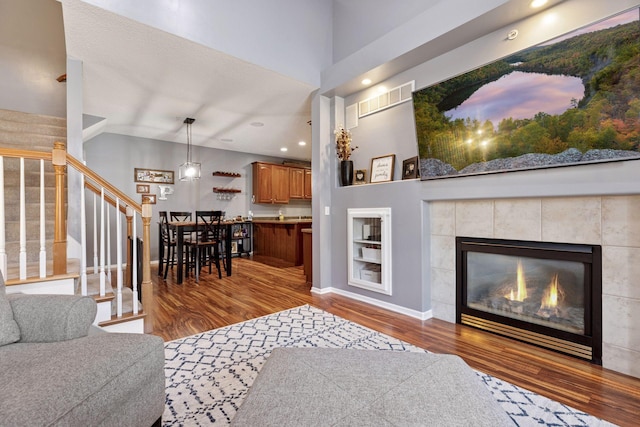 living area featuring visible vents, baseboards, stairway, a tile fireplace, and wood finished floors