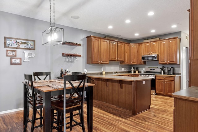 kitchen featuring a breakfast bar, light wood-style flooring, appliances with stainless steel finishes, a peninsula, and brown cabinetry