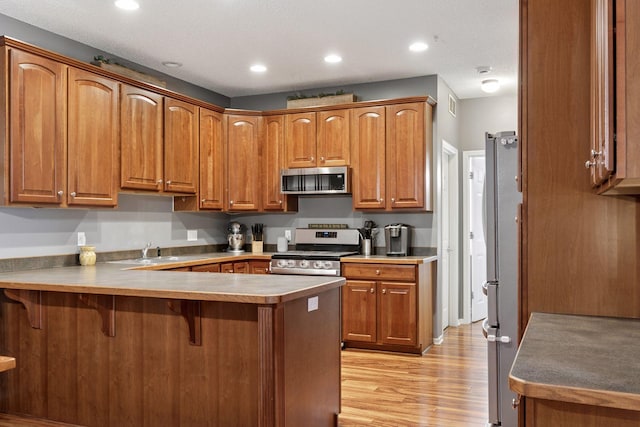 kitchen with brown cabinetry, a peninsula, appliances with stainless steel finishes, a kitchen breakfast bar, and light wood-type flooring