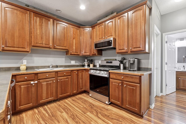 kitchen featuring brown cabinets, a sink, a textured ceiling, appliances with stainless steel finishes, and light wood finished floors