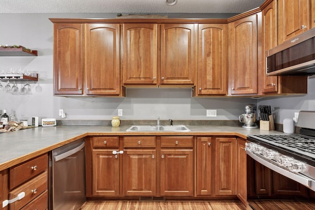 kitchen with a sink, brown cabinets, a textured ceiling, and appliances with stainless steel finishes