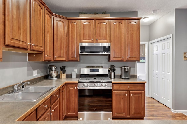 kitchen featuring brown cabinets, a textured ceiling, stainless steel appliances, and a sink