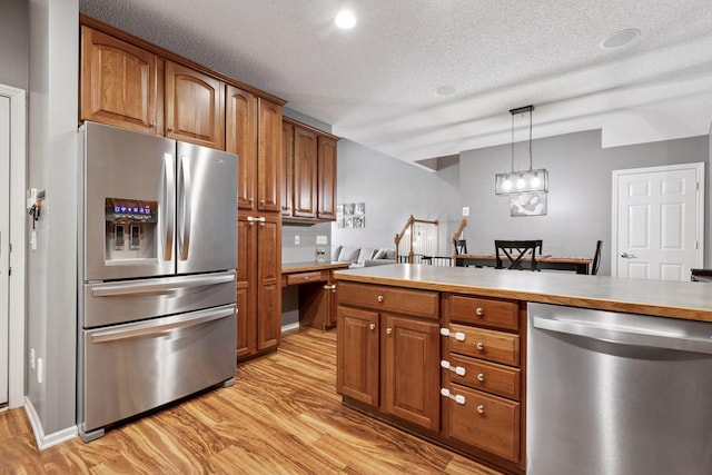 kitchen featuring light wood-style floors, appliances with stainless steel finishes, brown cabinetry, and built in study area