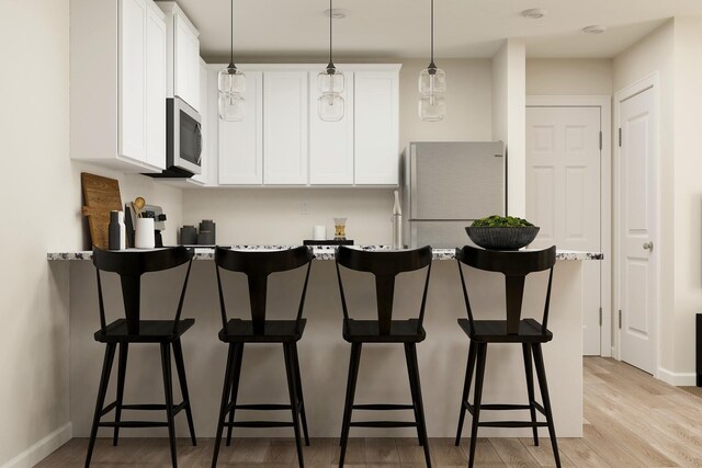 kitchen featuring light wood-type flooring, white cabinetry, a kitchen bar, and freestanding refrigerator