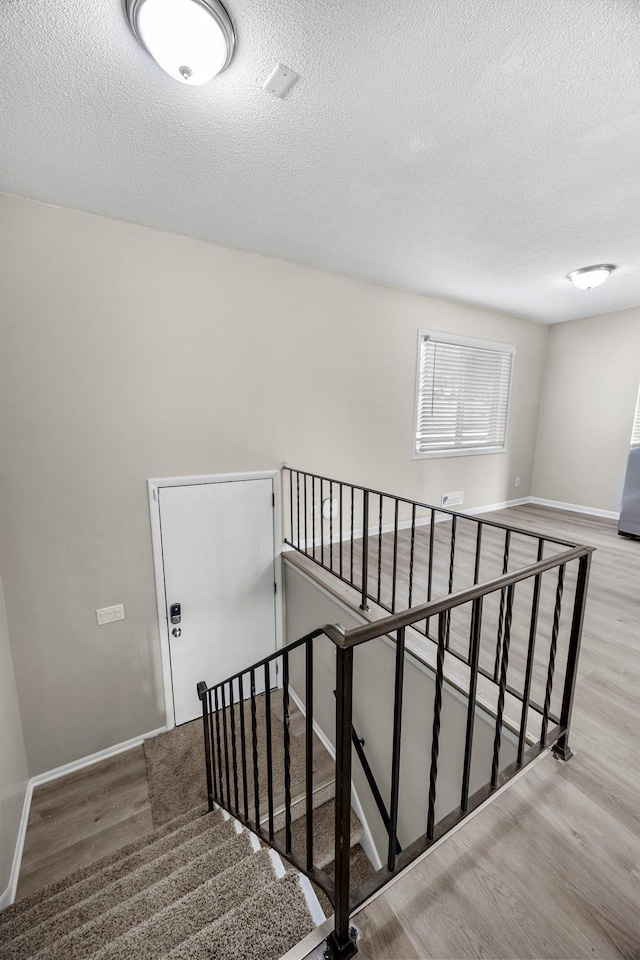 stairs with a textured ceiling, baseboards, and wood finished floors