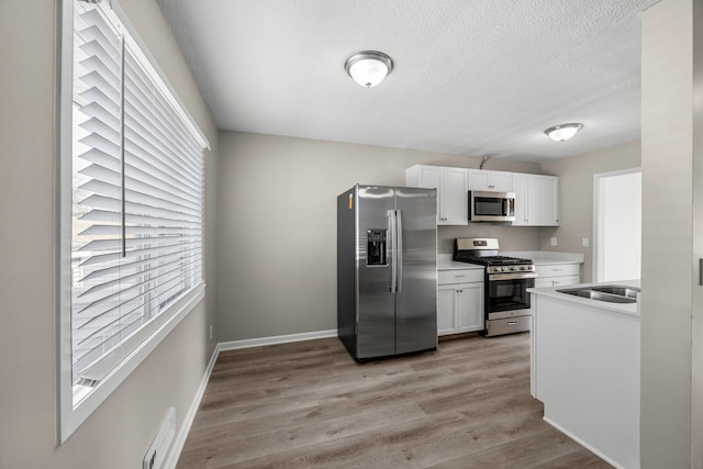 kitchen with light wood-type flooring, a sink, white cabinetry, appliances with stainless steel finishes, and baseboards