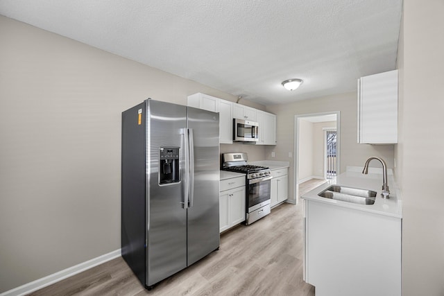 kitchen with a sink, stainless steel appliances, light wood finished floors, and white cabinetry