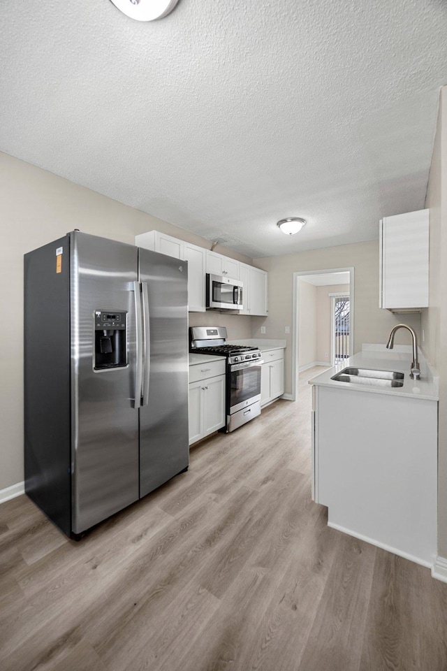 kitchen with light wood-type flooring, a sink, a textured ceiling, white cabinetry, and stainless steel appliances