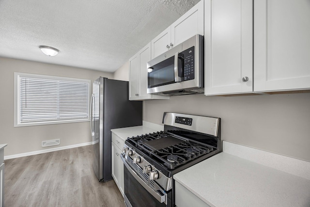 kitchen with light wood finished floors, appliances with stainless steel finishes, light countertops, and white cabinetry