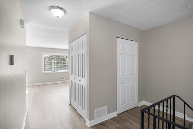 hall with visible vents, a textured ceiling, baseboards, and wood finished floors