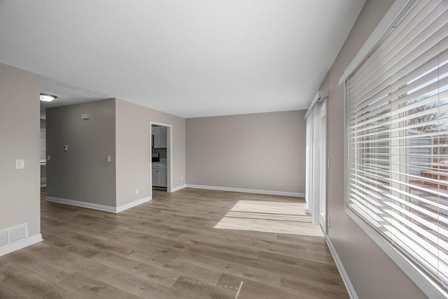 empty room with a textured ceiling, baseboards, visible vents, and light wood-type flooring