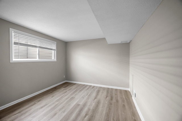 spare room with baseboards, a textured ceiling, and light wood finished floors