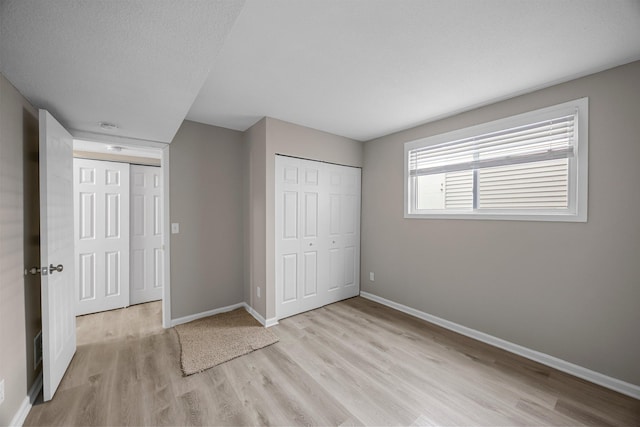 unfurnished bedroom featuring light wood-type flooring, baseboards, a textured ceiling, and a closet