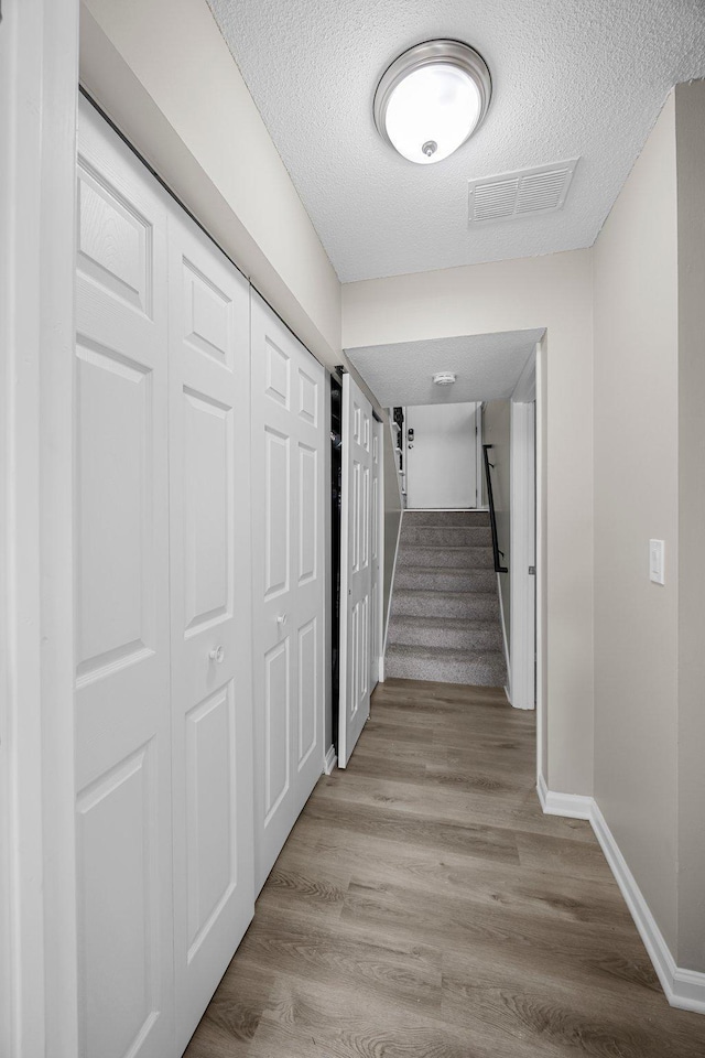 hall featuring baseboards, visible vents, stairs, a textured ceiling, and light wood-type flooring