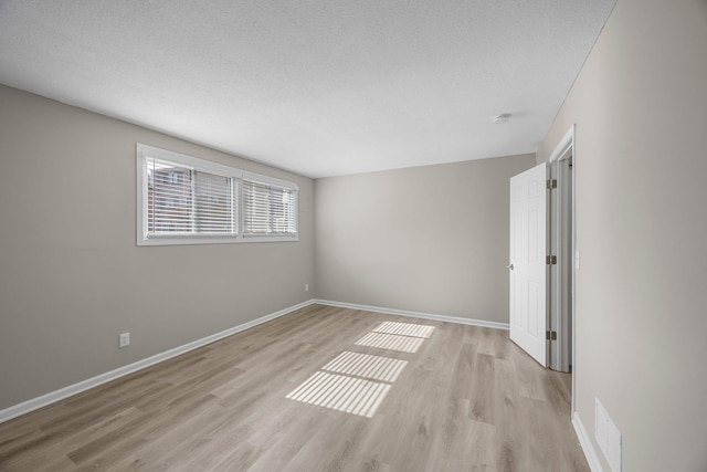 empty room with light wood finished floors, visible vents, a textured ceiling, and baseboards