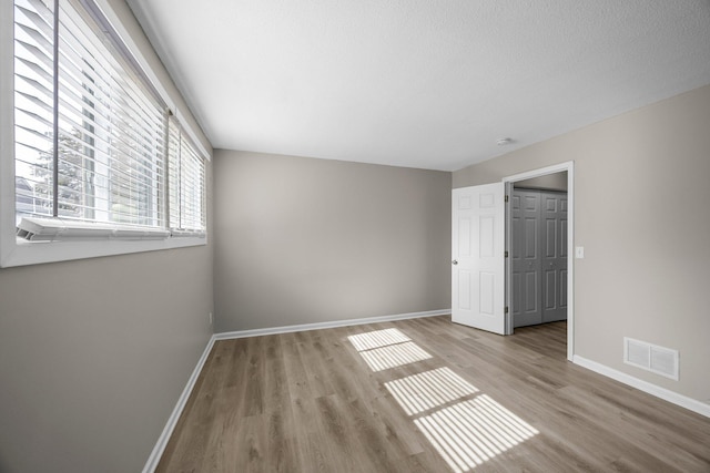 unfurnished bedroom featuring visible vents, a textured ceiling, baseboards, and wood finished floors