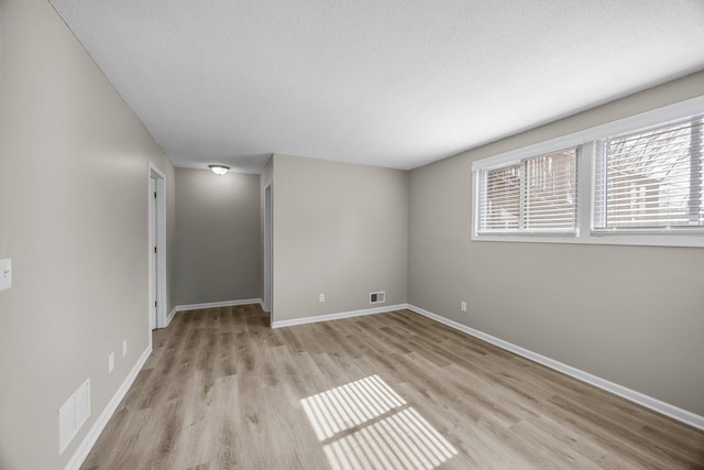 unfurnished room with a textured ceiling, baseboards, and light wood-style floors