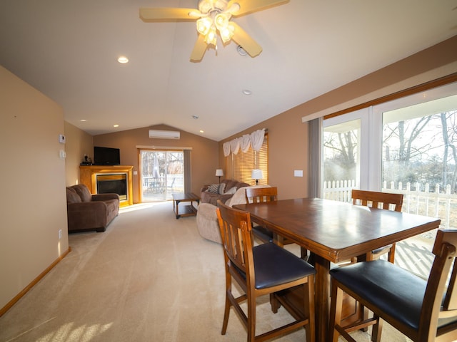 dining area with lofted ceiling, a wall unit AC, light carpet, a glass covered fireplace, and a ceiling fan