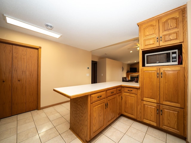 kitchen with white microwave, ceiling fan, light countertops, a peninsula, and light tile patterned flooring