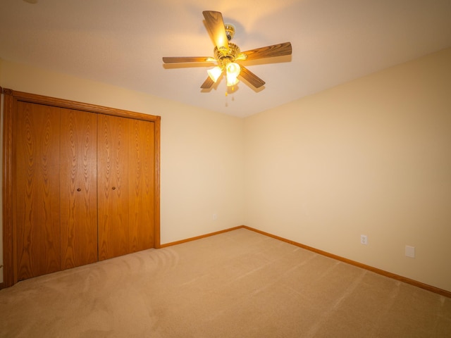 unfurnished bedroom featuring a ceiling fan, light colored carpet, baseboards, and a closet