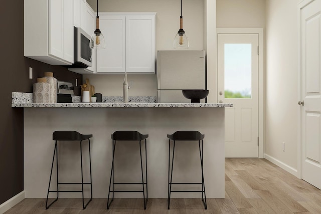 kitchen featuring stainless steel microwave, white cabinets, a kitchen bar, and light wood-style floors