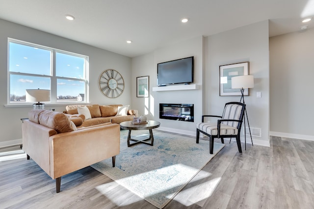 living area featuring recessed lighting, baseboards, a glass covered fireplace, and light wood-style flooring