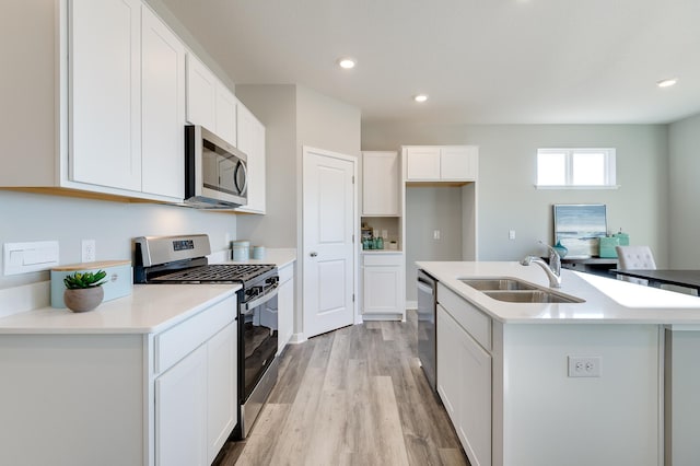 kitchen featuring an island with sink, a sink, white cabinetry, stainless steel appliances, and light wood finished floors